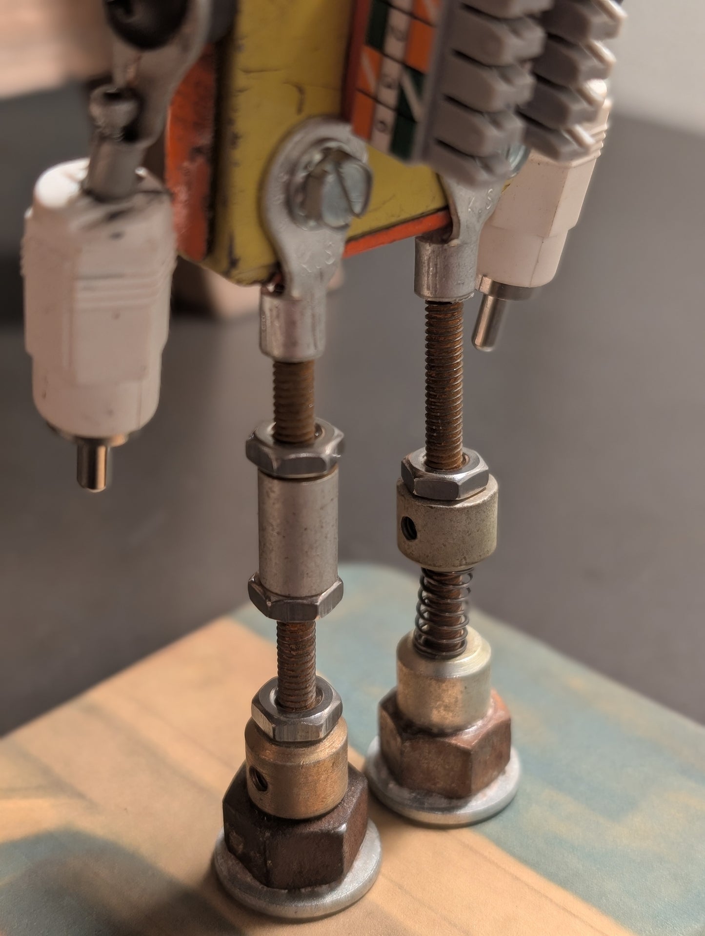 Three-view composite (front, leg detail, left profile) of the American Sentinel AF-5 robot sculpture, highlighting the threaded steel leg construction and vintage orange American Parts tin body.