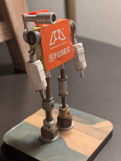 Handmade industrial robot sculpture made from a vintage orange American Parts fuse tin and upcycled RCA audio connectors on a wooden base.